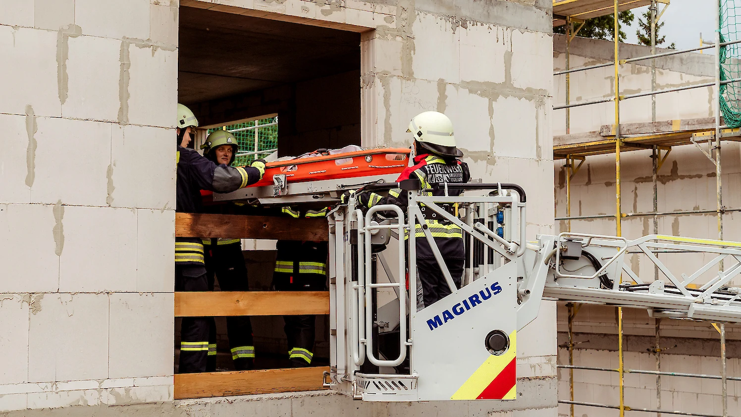 Feuerwehrkräfte retten einen Patienten mit Hilfe einer Drehleiter durch ein Gebäudefenster.