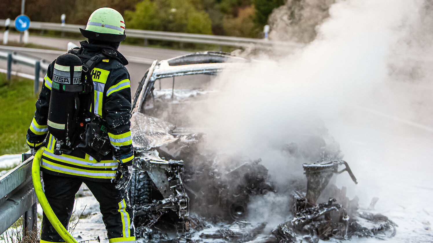 Ein Feuerwehrmann mit Atemschutzgerät steht vor den qualmenden Resten eines ausgebrannten PKW.