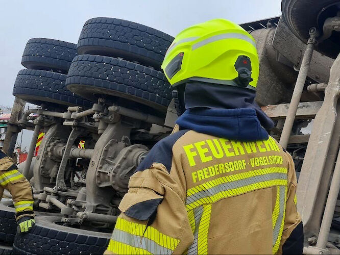 Ein Feuerwehrmann steht vor einem auf die Seite gekippten LKW.