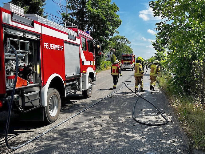 Feuerwehrkräfte bei Löscharbeiten am Seitenstreifen einer Straße.