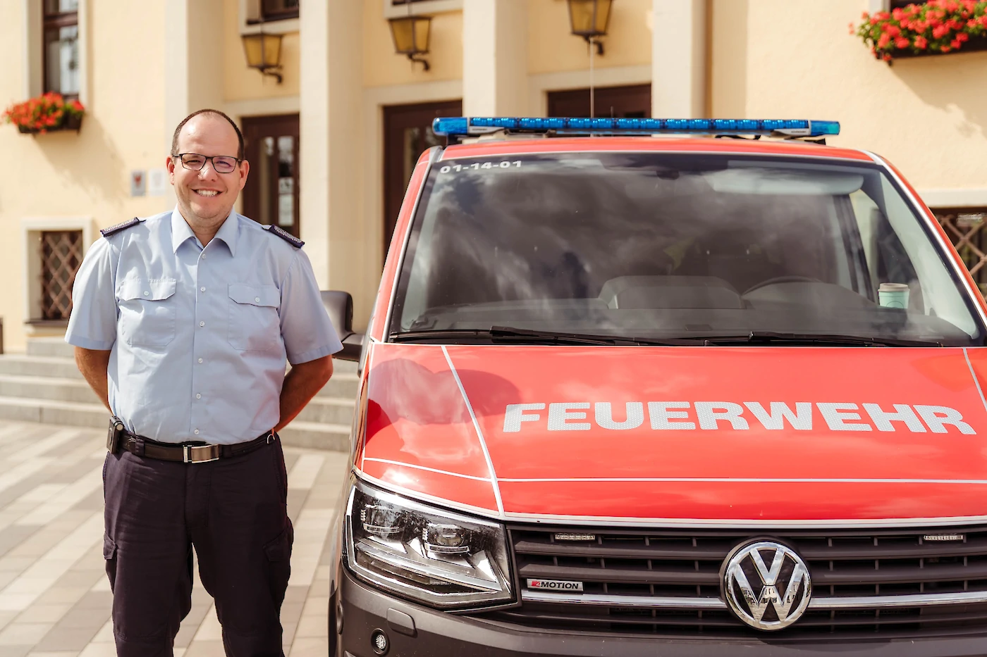 Thomas Rubin posiert in Uniform neben seinem Einsatzfahrzeug vor den Stufen des Rathauses.