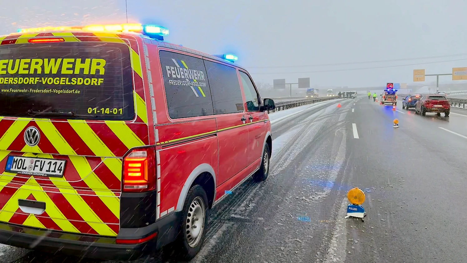 Ein Feuerwehrfahrzeug steht mit Blaulicht auf einer verschneiten Autobahn und sichert eine Unfallsstelle ab