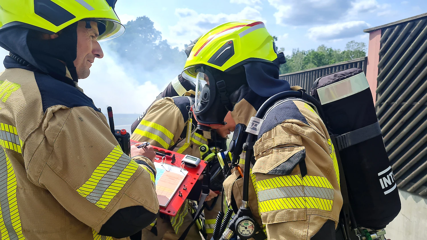 Ein Feuerwehrmann mit Atemschutzgerät neben einem Feuerwehrmann mit einer Schreibtafel in der Hand.