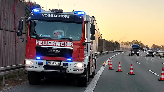 Ein Fahrzeug des Löschzugs Vogelsdorf steht mit Blaulicht auf der Autobahn, daneben einige Verkehrskegel und zwei PKW.